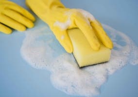 manos con guantes amarillos y una esponja limpiando una superficie con piedra blanca