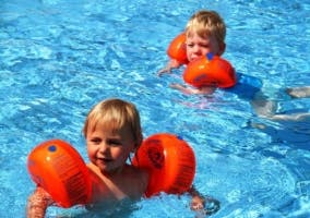 dos niños en la piscina con manguitos de natación color naranja