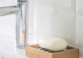 jabonera de bambú con una barra de jabón al lado de una llave de lavamanos